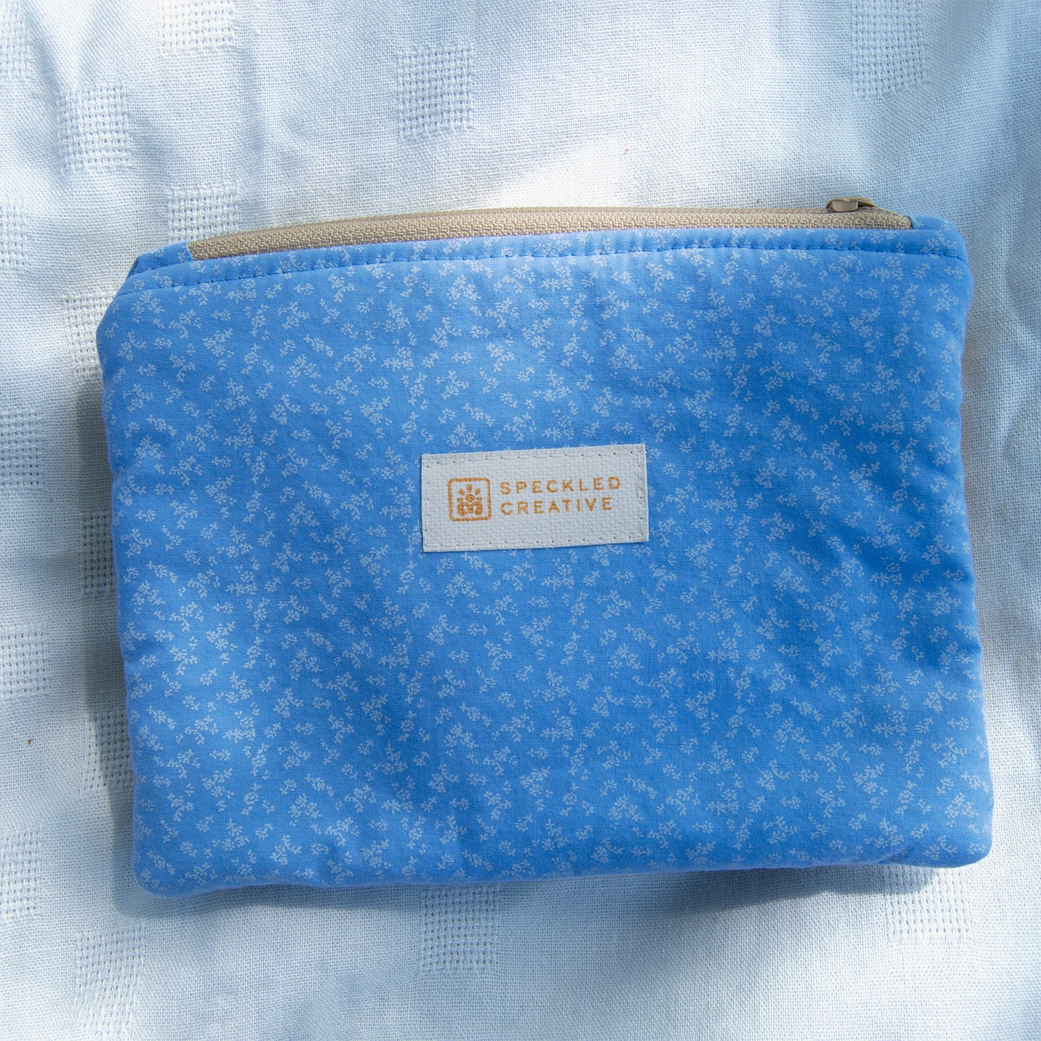 Blue pouch with a speckled pattern and a visible brand label on a light blue textured background.