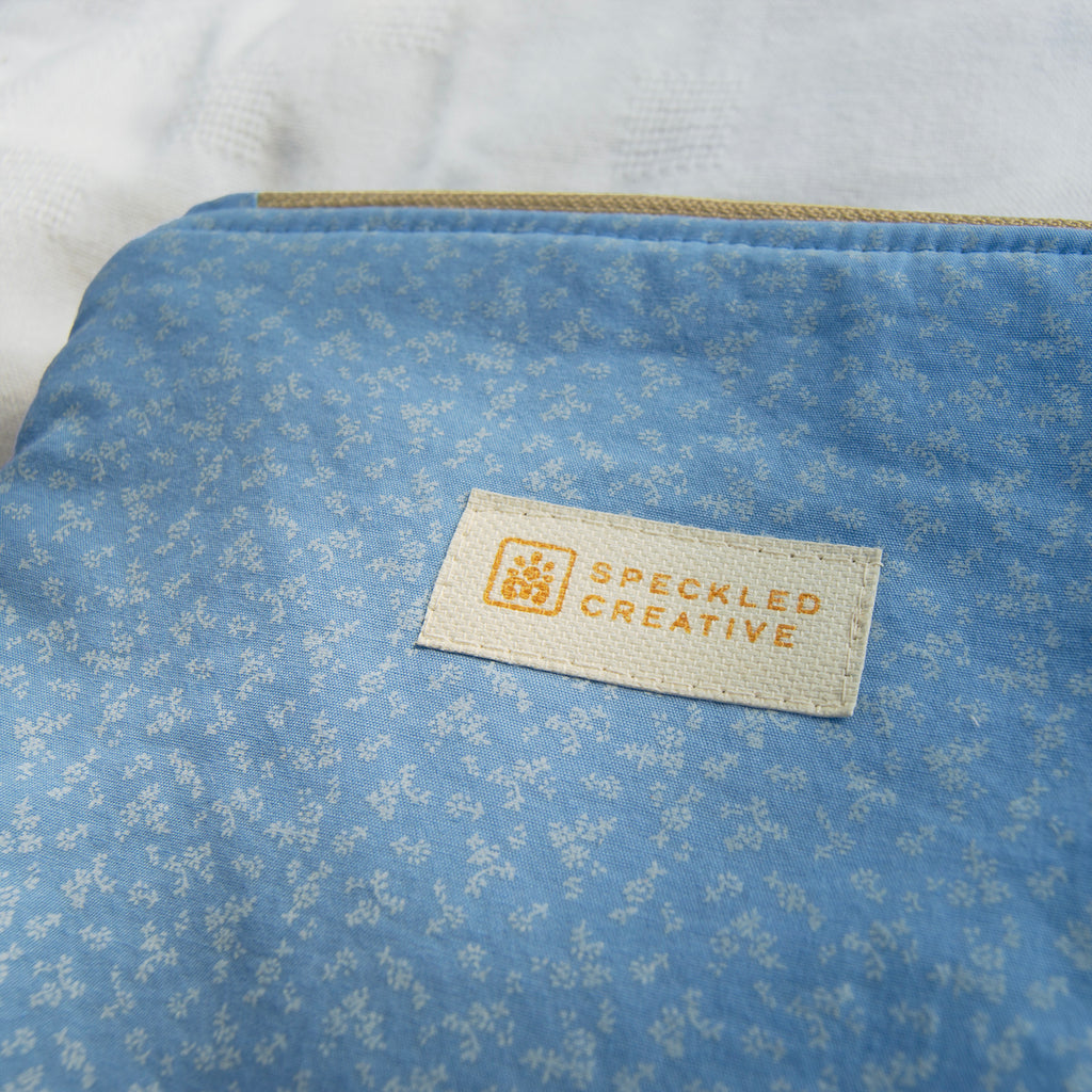 Blue fabric pouch with a subtle floral pattern and a Speckled Creative label on a white background