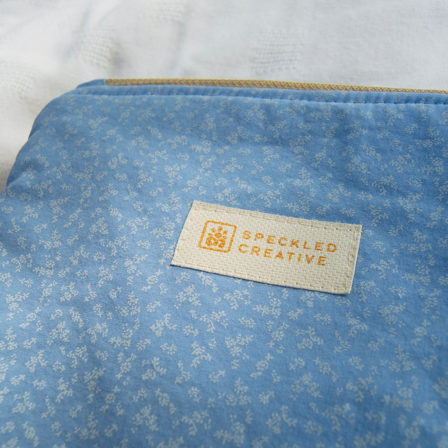 Blue fabric pouch with a subtle floral pattern and a Speckled Creative label on a white background