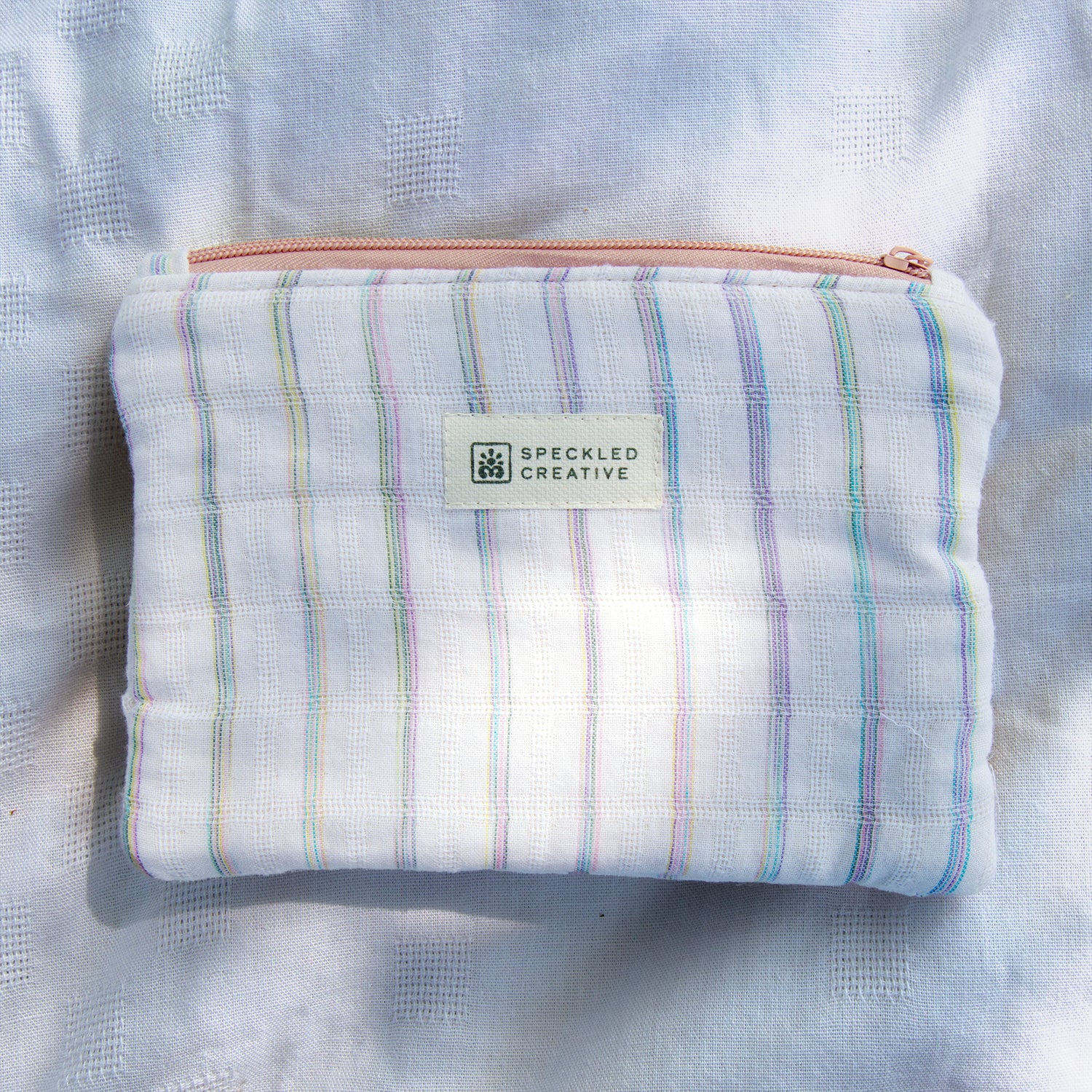 Striped pouch with a visible brand label on a textured fabric background