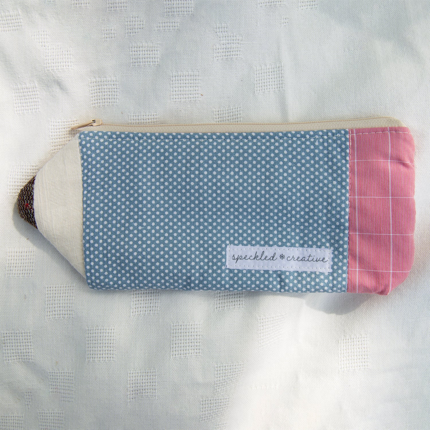 Fabric pouch shaped like a pencil with blue polka dot pattern and pink end on a white textured background