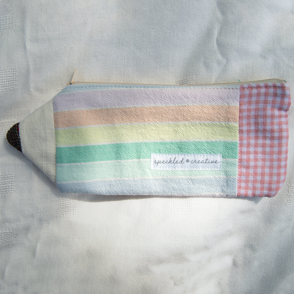 Multicolored striped pouch shaped like a pencil with a checkered eraser on a textured surface