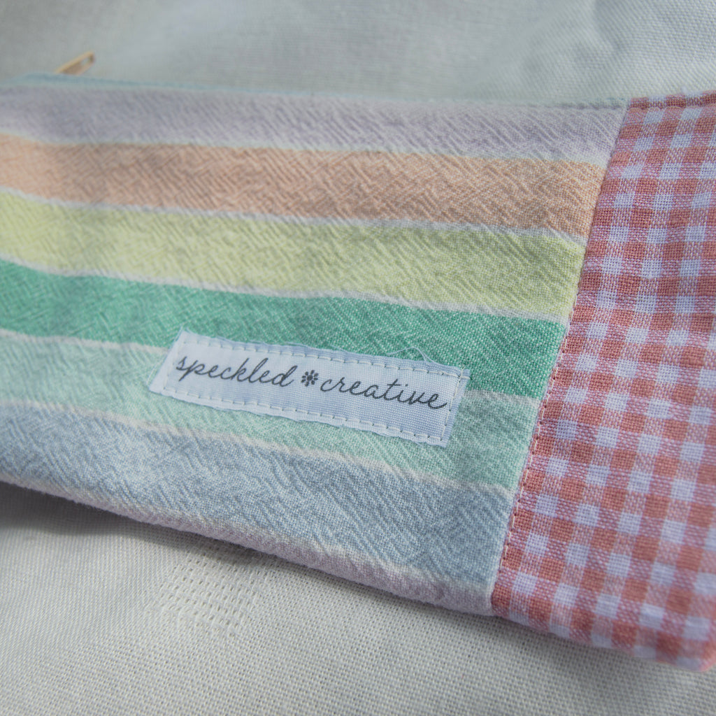 Pastel rainbow pouch shaped like a pencil  with a label reading 'speckled creative' on a checkered background