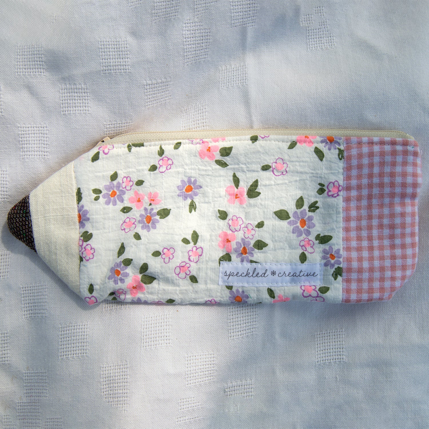 Floral patterned pouch shaped like a pencil with checkered end on a textured white background