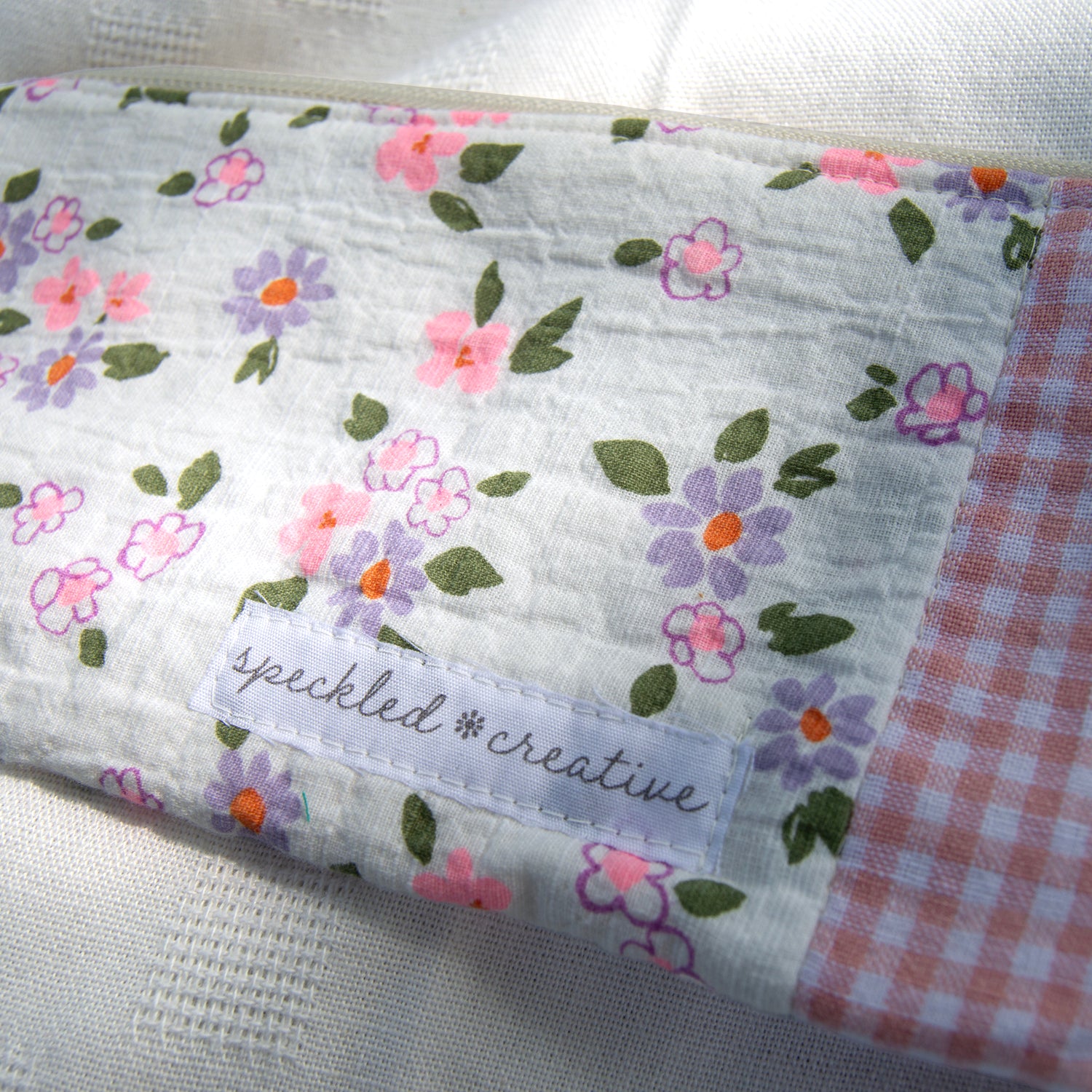 Close-up of a floral and checkered fabric pouch shaped like a pencil  with 'speckled creative' label