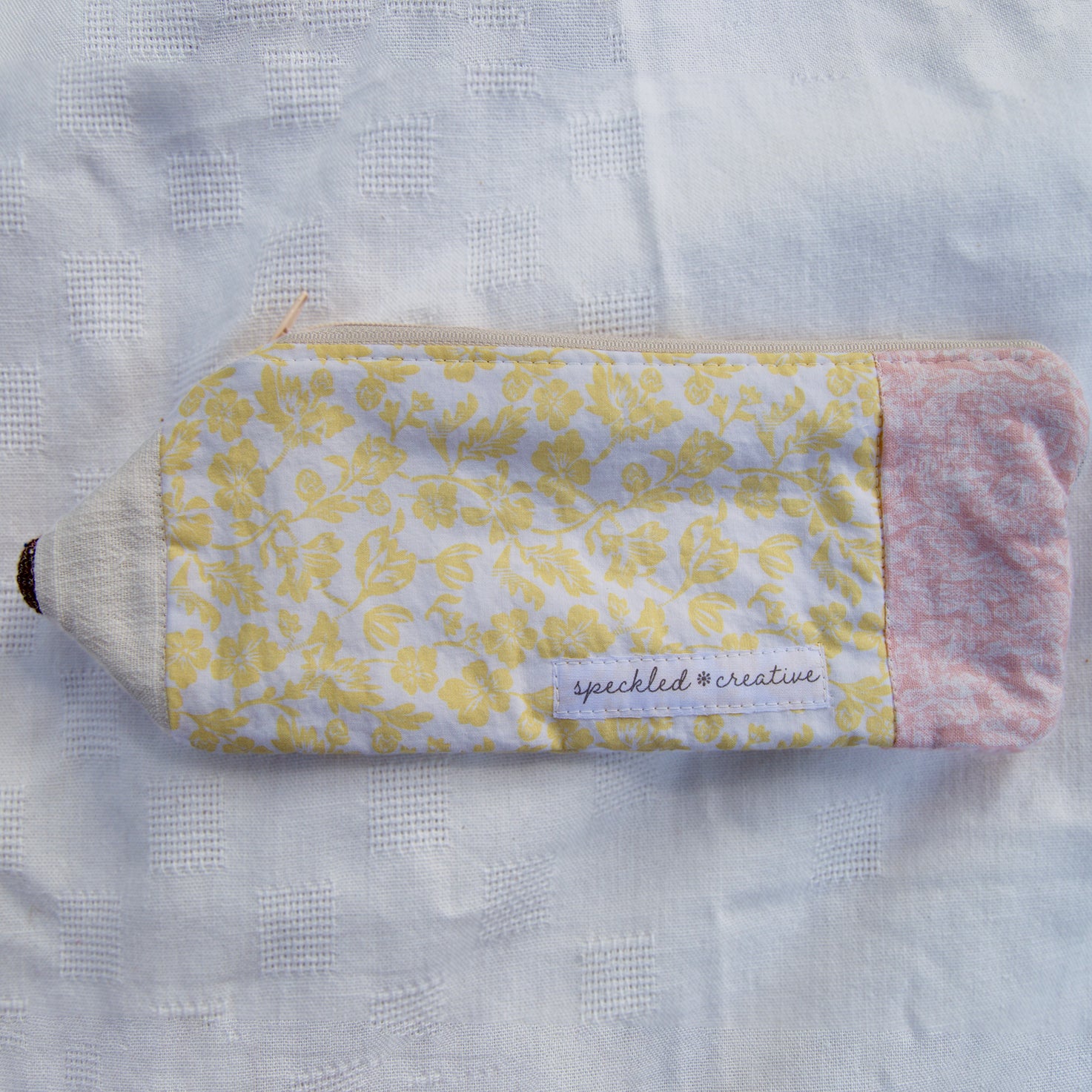 Floral-patterned pouch shaped like a pencil  with pink accents on a textured white background