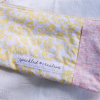 Close-up of a pouch shaped like a pencil with yellow and pink floral patterns and  'speckled creative' label on a light background