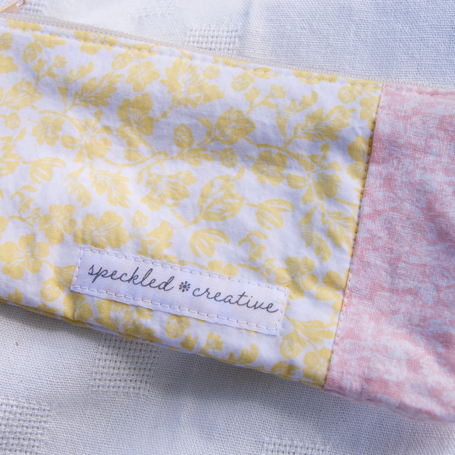 Close-up of a pouch shaped like a pencil with yellow and pink floral patterns and  'speckled creative' label on a light background