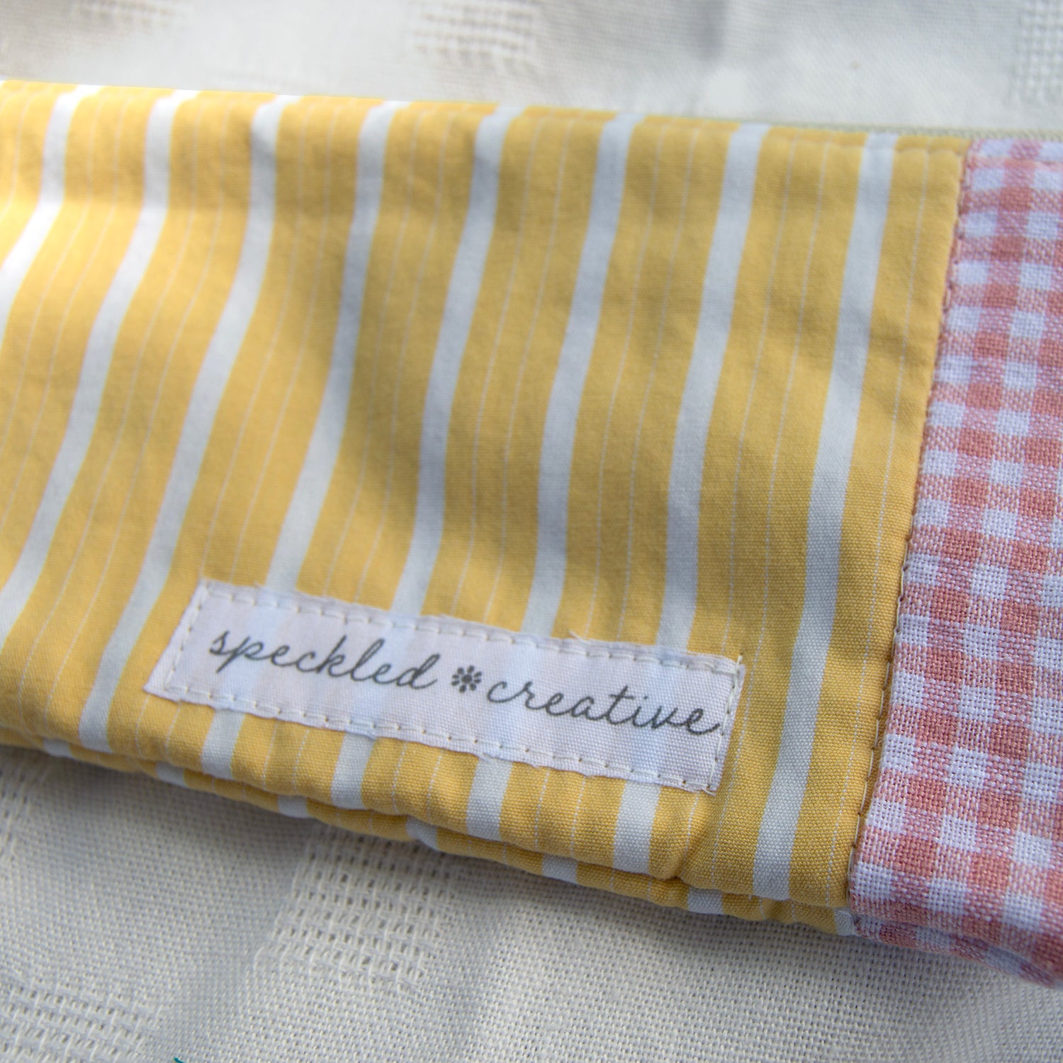 Yellow and white striped fabric with a checkered edge shaped like a pencil and 'speckled creative' label on a white background.