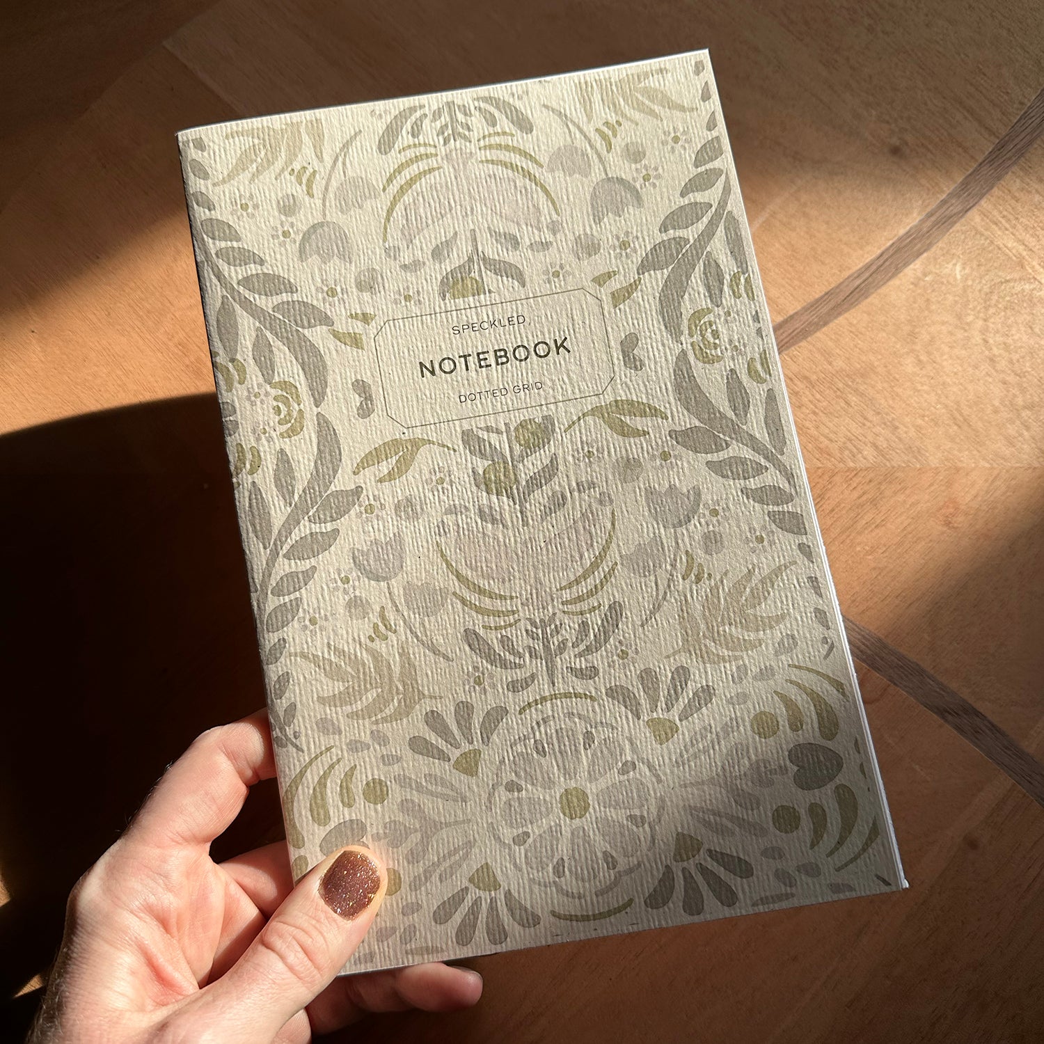 Floral-patterned notebook held by a hand on a wooden surface