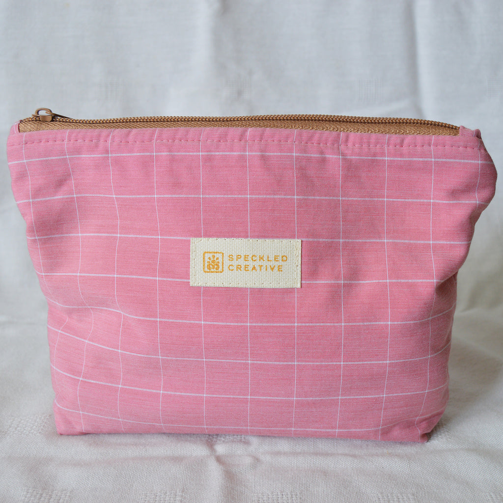 Pink checkered pouch with a gold zipper and 'Speckled Creative' label on a white background