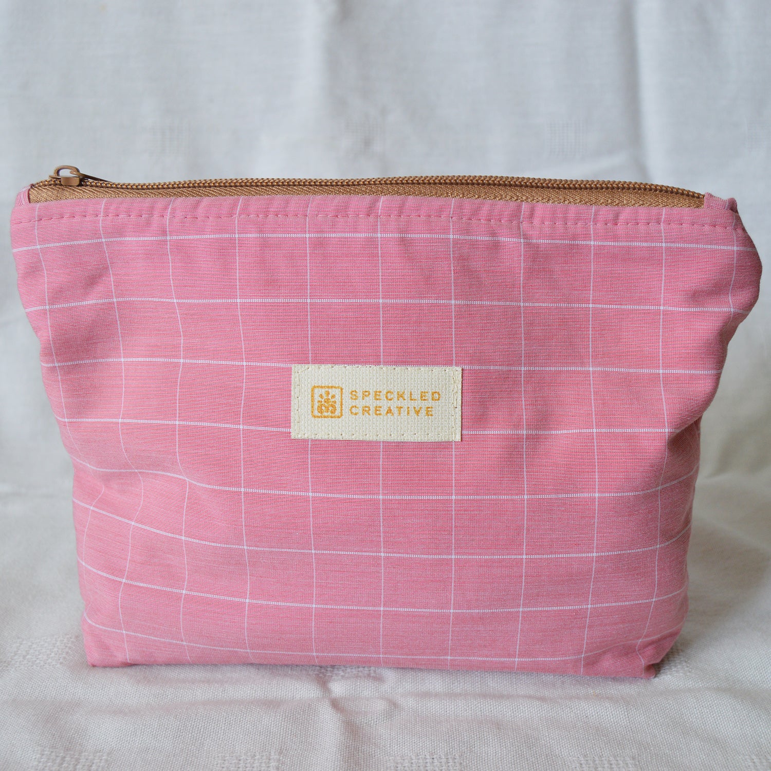 Pink checkered pouch with a gold zipper and 'Speckled Creative' label on a white background