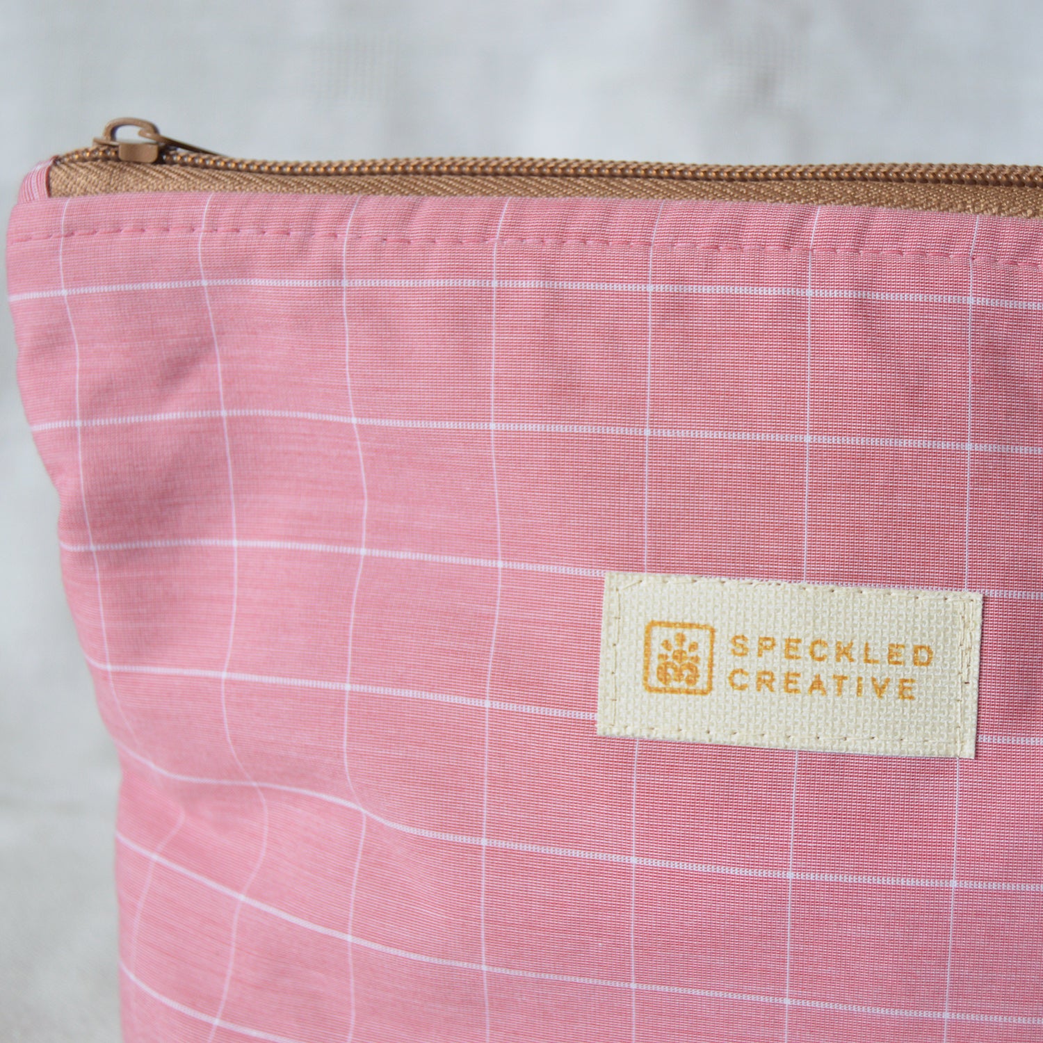 Close up of a pink checkered pouch with a Speckled Creative label on a light gray background