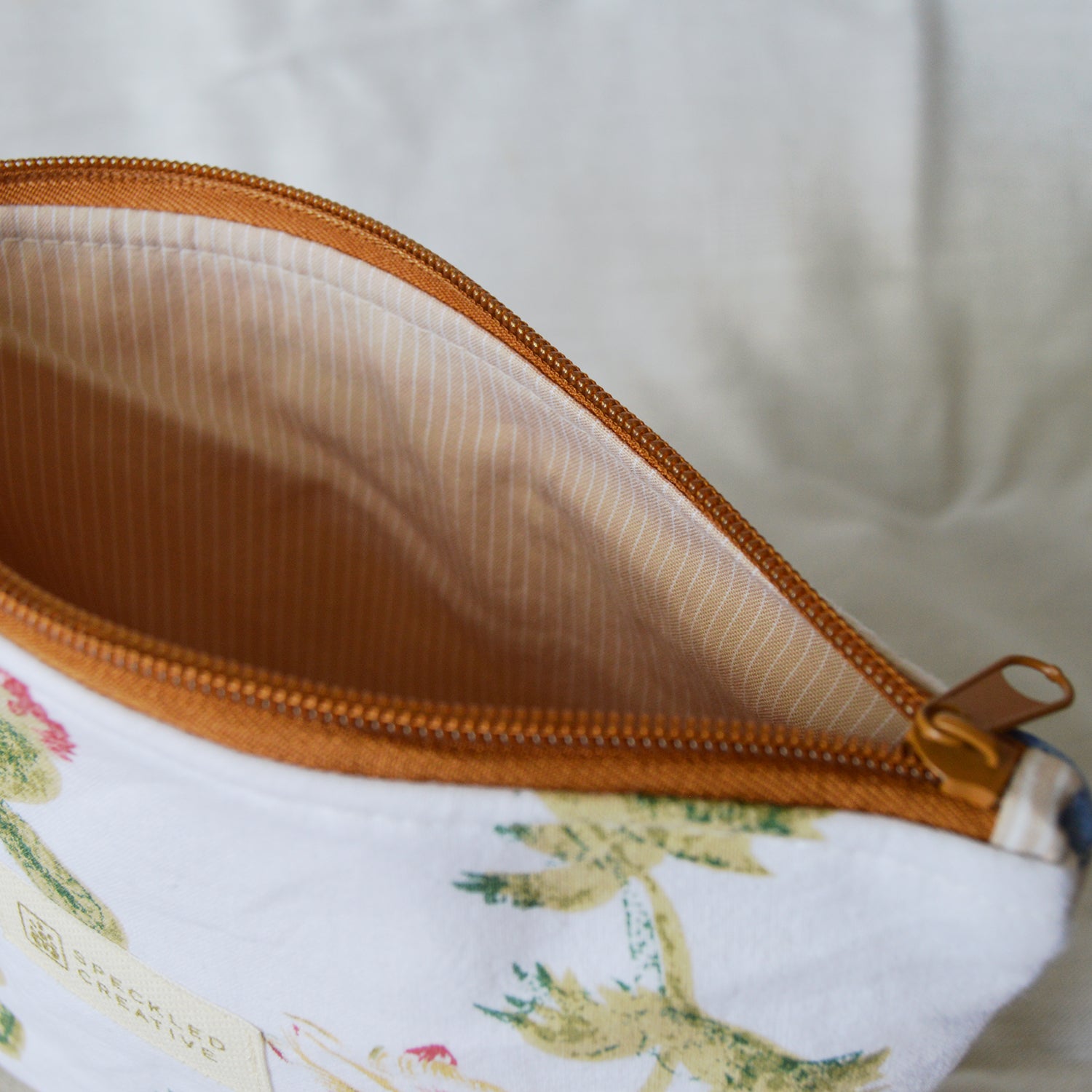 Close-up of a pouch with a floral pattern and brown zipper on a light background