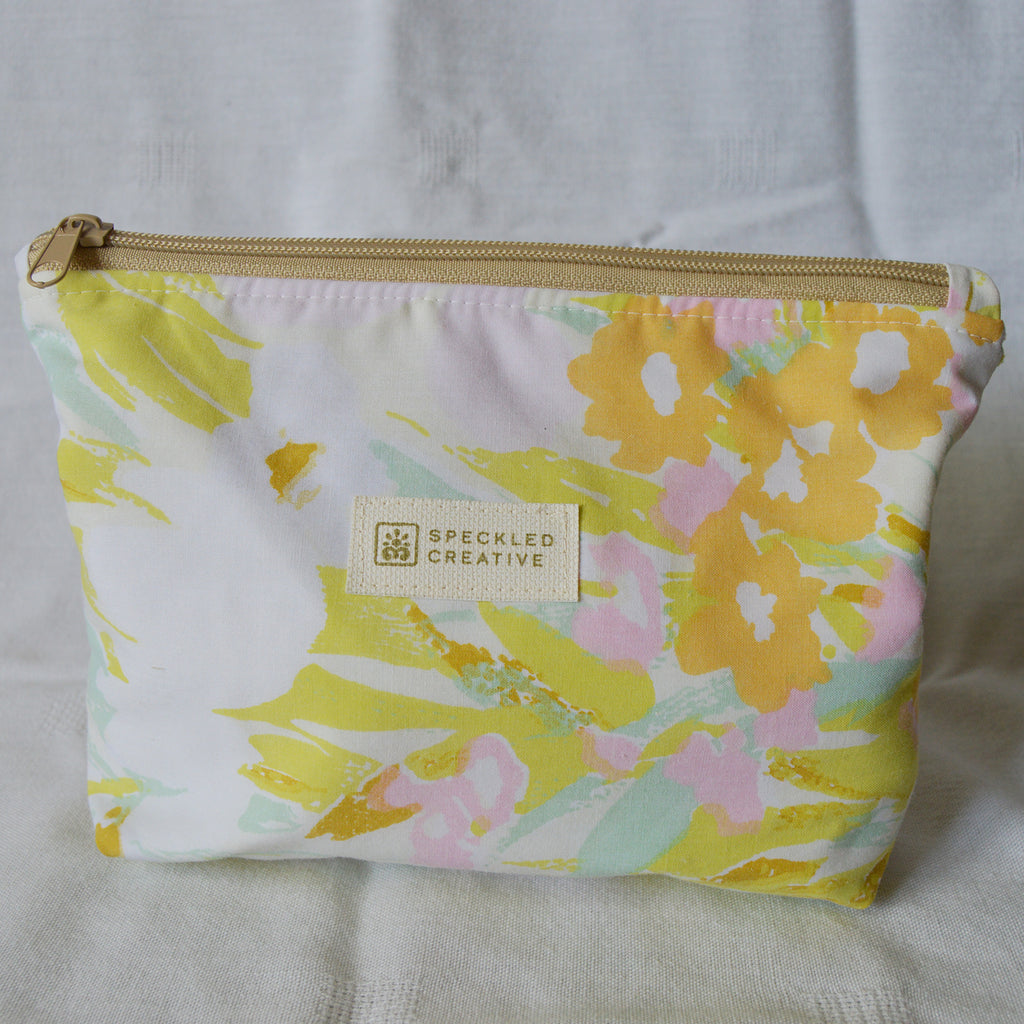 Floral-patterned pouch with gold zipper on a light gray background