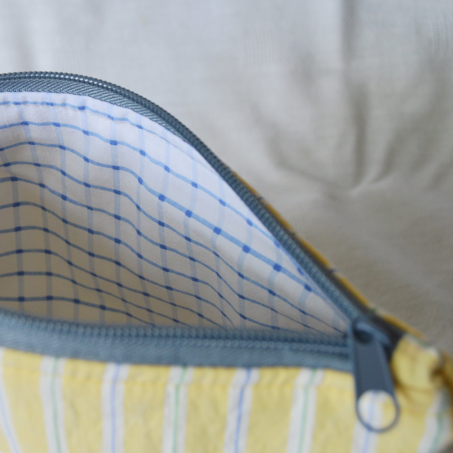 Close-up of a yellow fabric pouch with a blue zipper on a neutral background